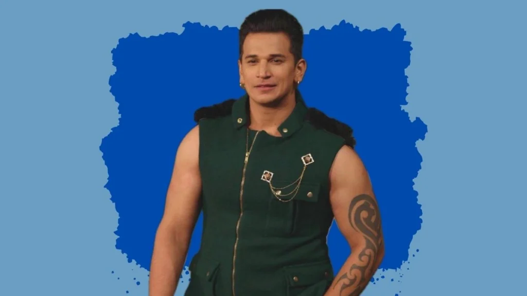 Prince Narula: Stylish Man in a Sleeveless Green Jacket with Accessories Prince Narula wearing a sleeveless green jacket with decorative chains, posing against a blue background
