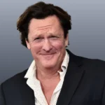 A headshot of actor Michael Madsen Death - Hollywood Says Goodbye to a Relentless Icon, a middle-aged man with dark, slightly wavy hair, a faint smile, and a white polka-dot shirt under a dark jacket, against a grey background.