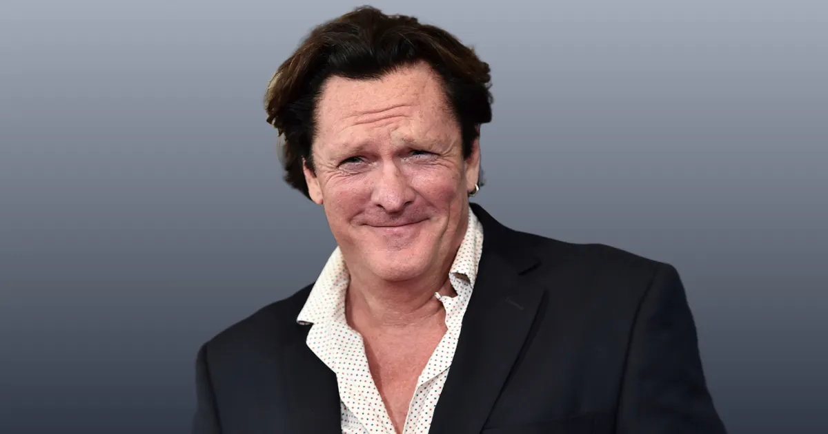 A headshot of actor Michael Madsen Death - Hollywood Says Goodbye to a Relentless Icon, a middle-aged man with dark, slightly wavy hair, a faint smile, and a white polka-dot shirt under a dark jacket, against a grey background.