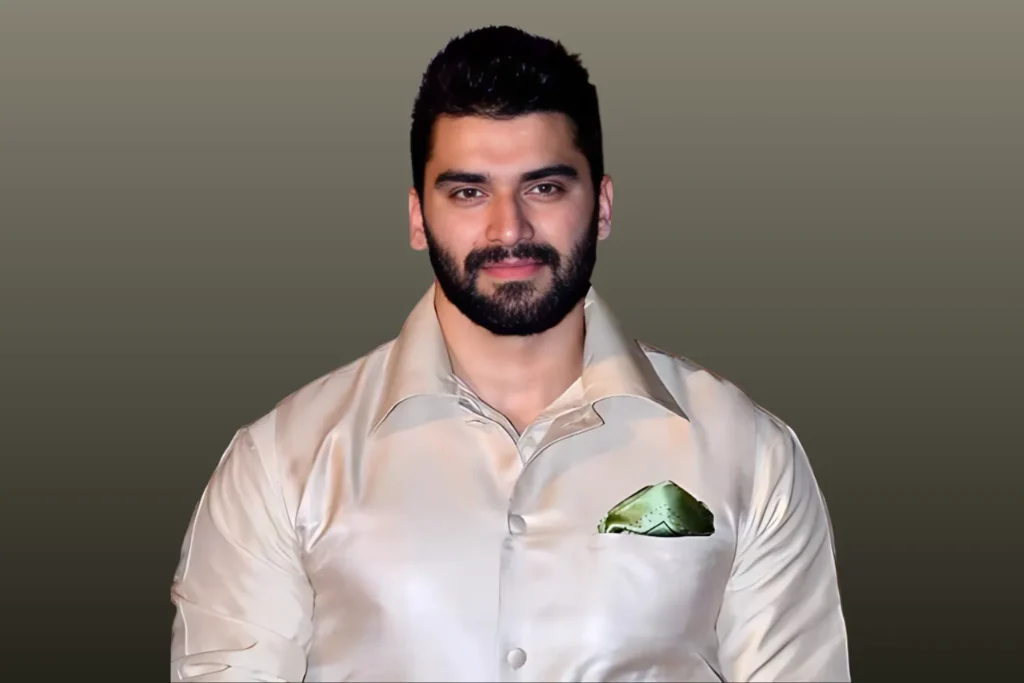 Portrait of a man in a shiny cream-colored formal shirt with green pocket square on a muted grey background; a representation of Nikitin Dheer’s legacy and journey.