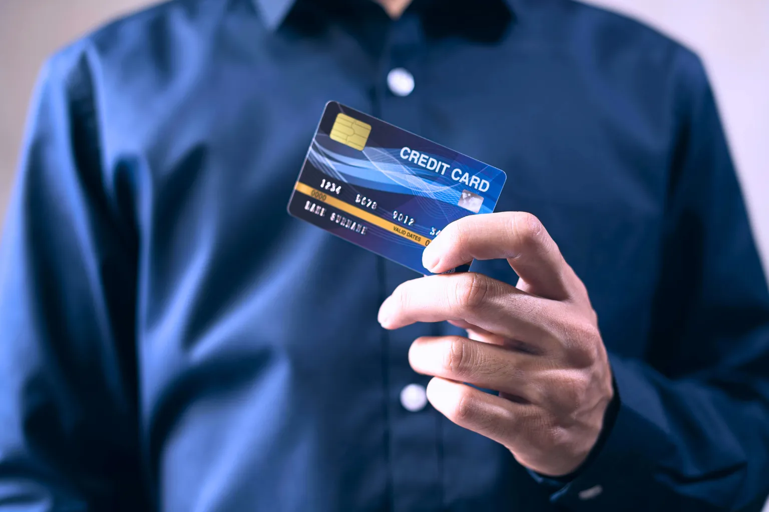 A hand in a blue shirt holds a chip-enabled credit card, representing the best credit cards in India for 2026 to maximize savings.